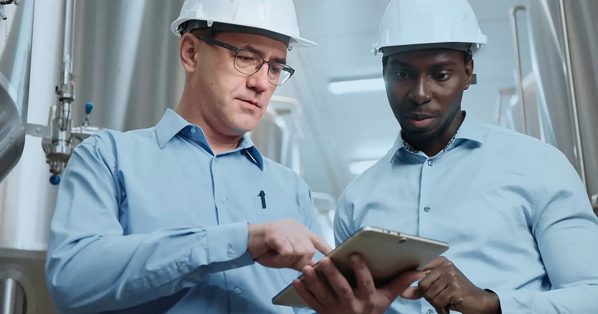 Two engineers in hard hats reviewing an inspection on a tablet