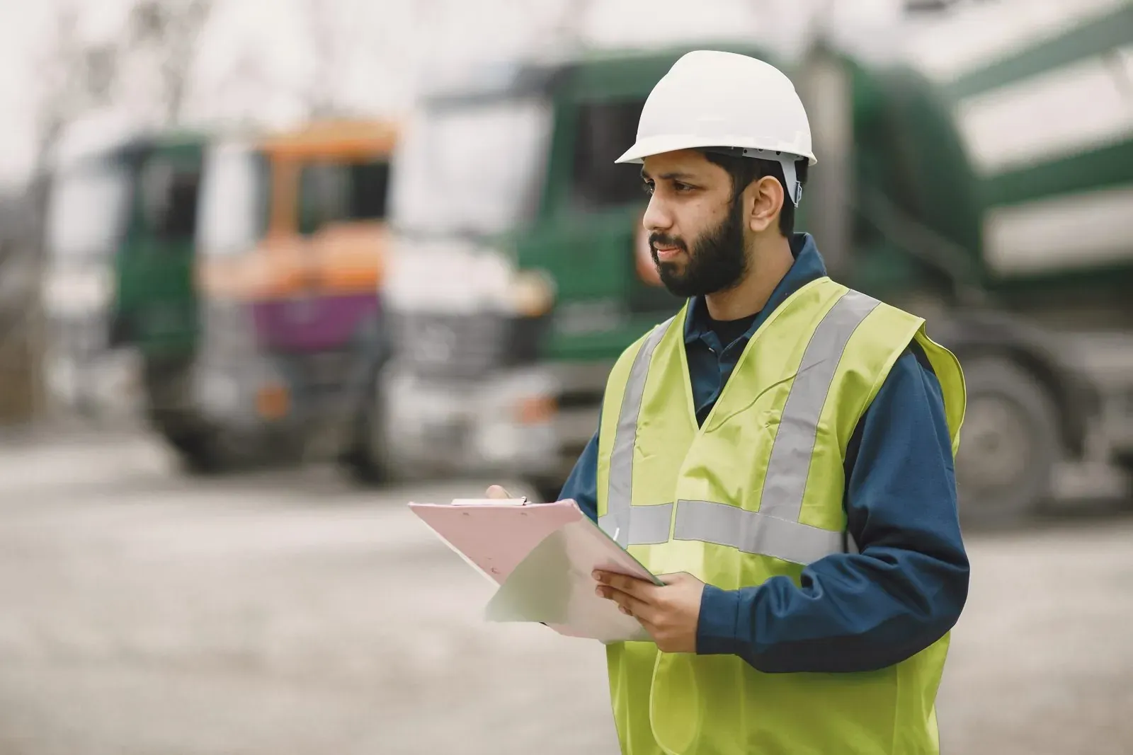 Safety inspector in a hard hat checking a clipboard beside a truck fleet